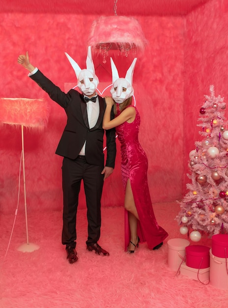 La pareja con máscaras poligonales de conejo en el fondo rosa está celebrando el Año Nuevo 2023. C