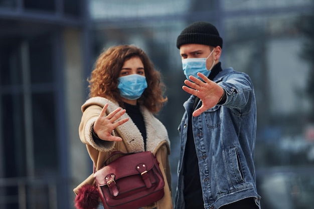 Una pareja con máscaras protectoras da un paseo al aire libre en la ciudad cerca del edificio comercial en tiempo de cuarentena Concepción del coronavirus