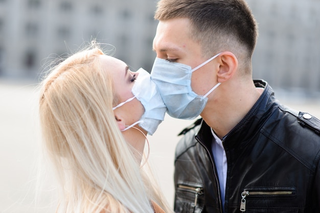 Pareja en máscaras protectoras tiene un paseo al aire libre en la ciudad cerca del edificio de negocios en el momento de la cuarentena. Concepción de coronavirus.