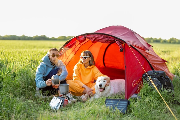 Pareja y mascota en camping con carpa en un campo verde