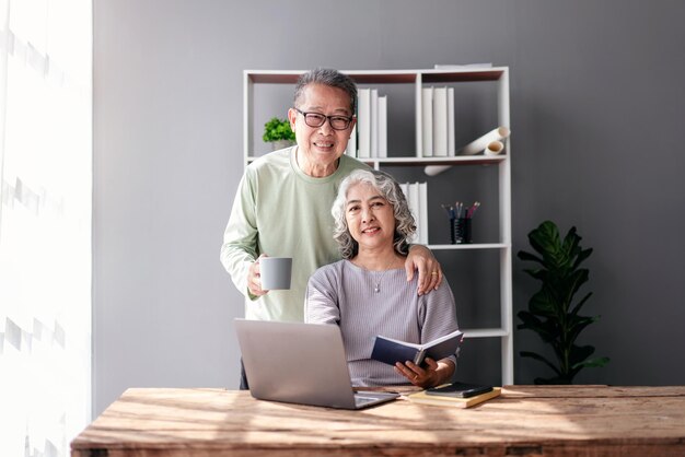 Pareja mayor bebiendo café y abrazándose para mirar la cámara mientras lee información en la computadora portátil