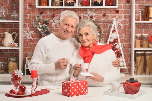 Pareja mayor bebiendo café con adornos navideños en el fondo