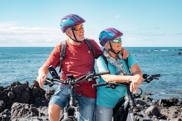 Pareja mayor caucásica de ciclistas con cascos descansando en la playa con bicicletas eléctricas disfrutando de un día soleado Auténtico concepto de vida jubilado para personas mayores Horizonte sobre el mar