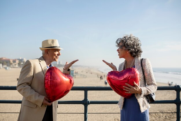 Pareja mayor enviándose besos al aire mientras sostiene globos en forma de corazón en una cita