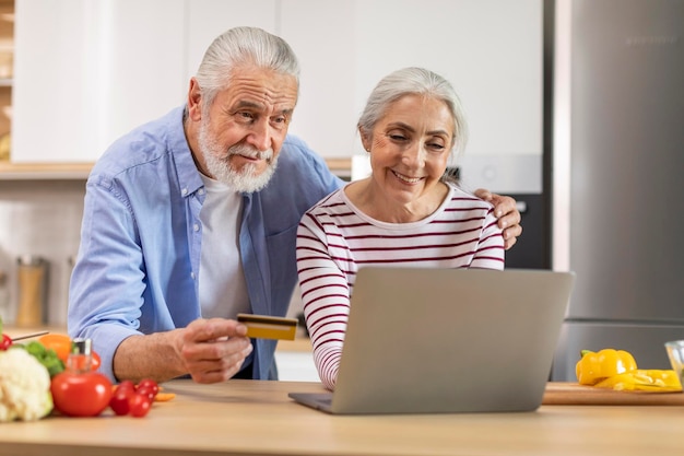 pareja mayor, pedido, comestibles, en línea, con, computador portatil, y, tarjeta de crédito, en, cocina