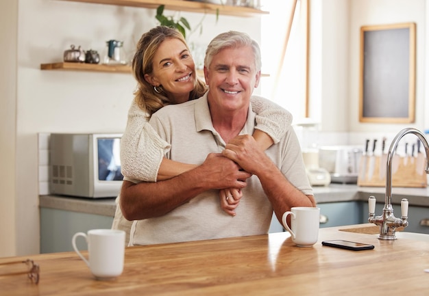 Pareja mayor sonríe y ama mientras se abraza en la cocina bebiendo café relajarse y vincularse sintiéndose feliz apoyo y confianza Retrato del viejo hombre y mujer de Australia en una relación o matrimonio saludable