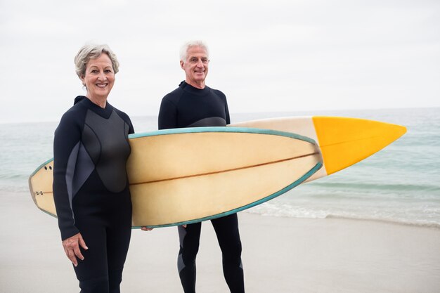 Pareja mayor, con, tabla de surf, posición, en la playa