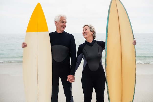 Pareja mayor, con, tabla de surf, tenencia, mano, en la playa