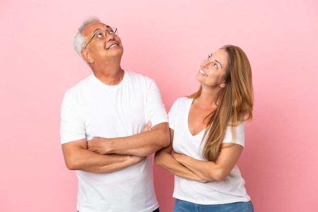 Pareja de mediana edad aislada sobre fondo rosa mirando hacia arriba mientras sonríe