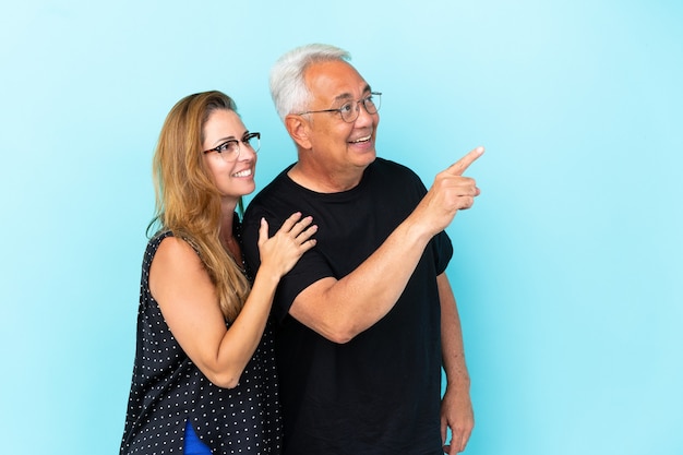 Pareja de mediana edad aislado sobre fondo azul apuntando con el dedo hacia un lado y presentando un producto