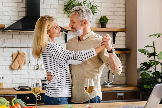 Una pareja de mediana edad bailando en la cocina de casa.