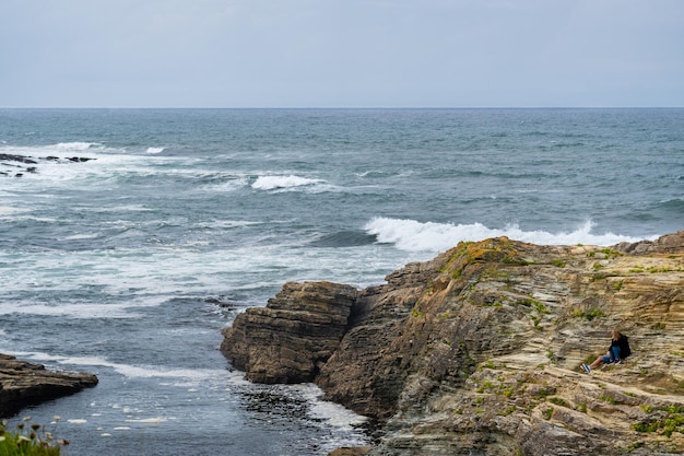 Pareja de mediana edad de hombre y mujer contemplando el Océano Atlántico sentado en una cornisa de rocas