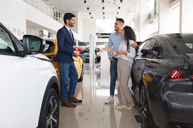 Pareja del medio oriente conversando con asistente de ventas comprando auto