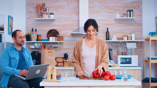 La pareja mira la receta en la computadora portátil en la cocina para ensalada orgánica. Marido y mujer cocinando comida receta. Feliz estilo de vida saludable juntos. Familia en busca de comida en línea. Ensalada fresca saludable