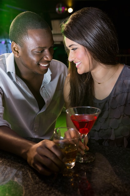 Pareja mirando el uno al otro y sonriendo mientras toma una copa en el bar