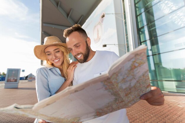 Foto pareja mirando el mapa contra el edificio de la terminal del aeropuerto