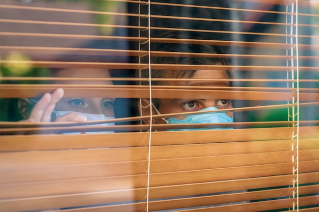 Pareja mirando por la ventana y usando máscara de protección y recuperación de la enfermedad en el hogar. Cuarentena.