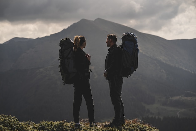 La pareja con mochilas de pie sobre un fondo de paisaje de montaña