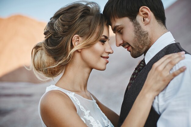 Pareja de moda y hermosa, feliz modelo rubia con peinado elegante, con un vestido de encaje blanco y un hombre guapo con estilo en el traje de moda