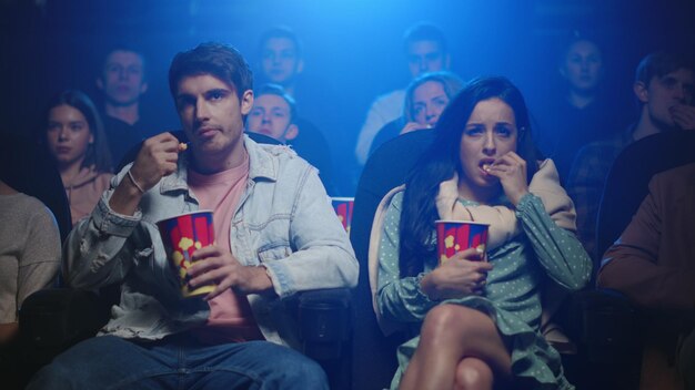 Foto pareja molesta viendo melodrama en el cine mujer preocupada secándose las lágrimas en el cine oscuro gente triste comiendo palomitas de maíz de cajas interiores