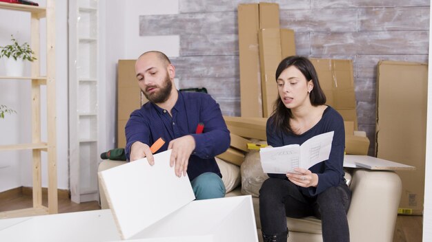 Pareja montando muebles siguiendo las instrucciones en su nuevo apartamento. Pareja trabajando en equipo.