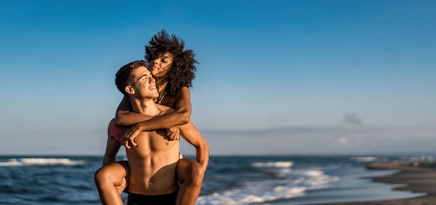 Pareja multicultural de jóvenes amantes piggybacking en la playa