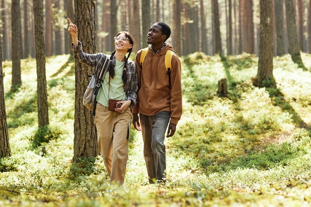 Pareja multiétnica mirando la hermosa naturaleza mientras caminan juntos en el bosque
