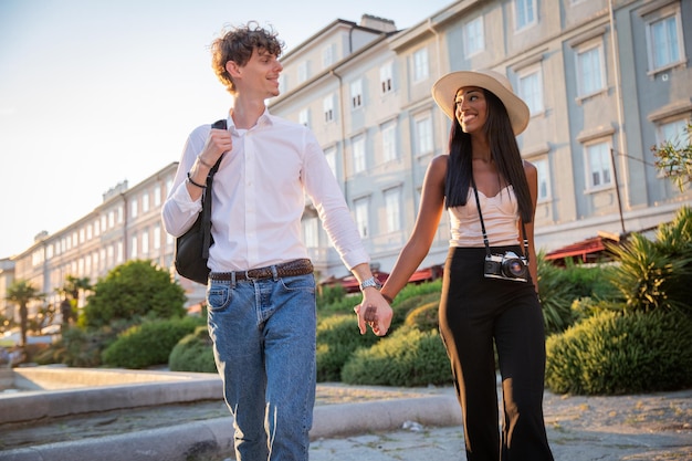 Una pareja multiétnica de vacaciones tomados de la mano y paseando por el centro de la ciudad