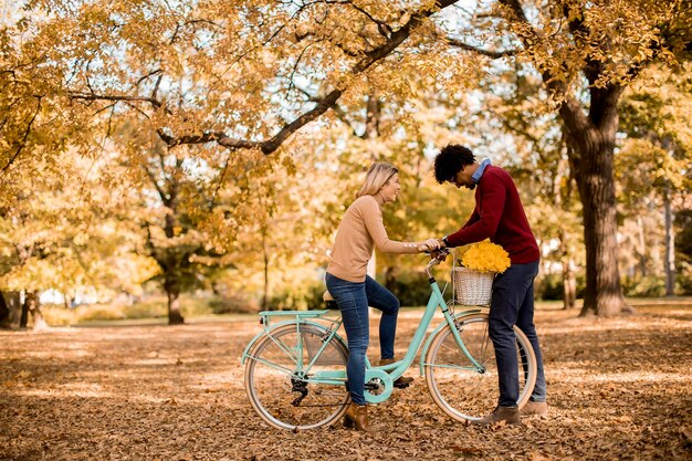 Pareja multirracial con bicicleta en el parque de otoño