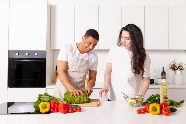 Pareja multirracial en la cocina preparando ensalada juntos chico americano y chica preparando comida vegetariana