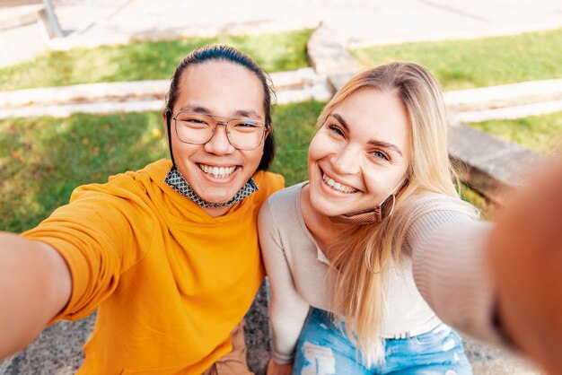 Pareja multirracial con mascarilla protectora tomando un selfie al aire libre