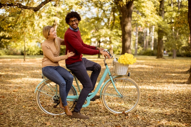 Pareja multirracial montando en bicicleta en el parque otoño