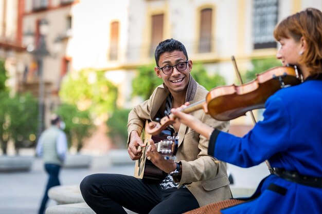 Pareja de músicos tocando y divirtiéndose en la calle. Guitarrista latino y violinista caucásico.