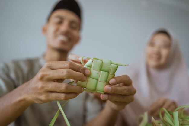 Pareja musulmana asiática haciendo pastel de arroz ketupat en casa usando hoja de palma