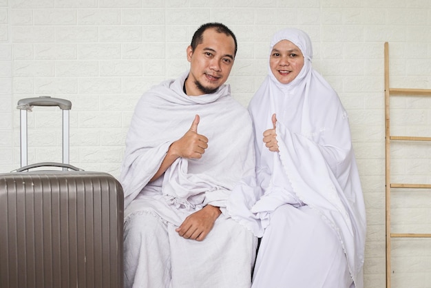 Pareja musulmana asiática vestida con ropa blanca de ihram, sentada mientras da el visto bueno