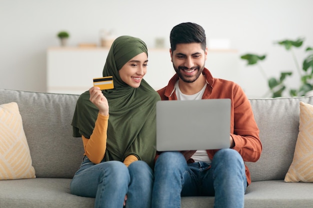 Pareja musulmana comprando en línea a través de una computadora portátil y una tarjeta de crédito en el interior