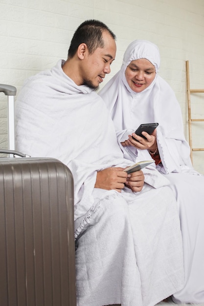 Pareja musulmana hajj o umrah usando ihram blanco islámico mientras usa un teléfono inteligente