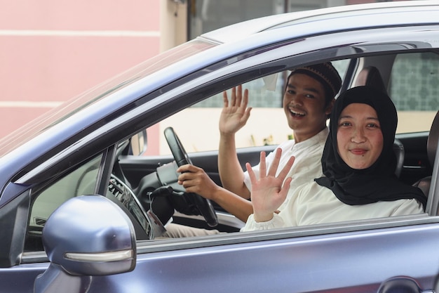 Pareja musulmana sonríe y agita la mano dentro del auto lista para irse de vacaciones o mudik lebaran