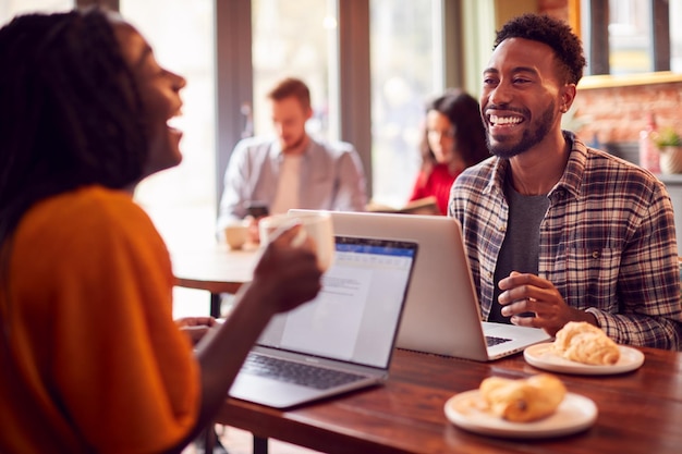 Pareja de negocios con computadoras portátiles que tienen una reunión informal en la cafetería