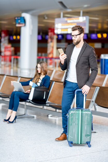 Pareja de negocios elegante sentado con laptop, teléfono y maleta en la sala de espera en el aeropuerto. Concepto de viajes de negocios