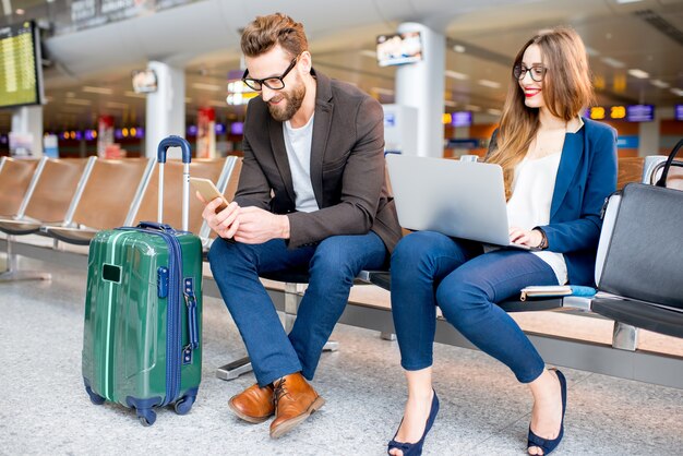 Pareja de negocios elegante trabajando con ordenador portátil y teléfono sentado en la sala de espera en el aeropuerto. Concepto de viajes de negocios