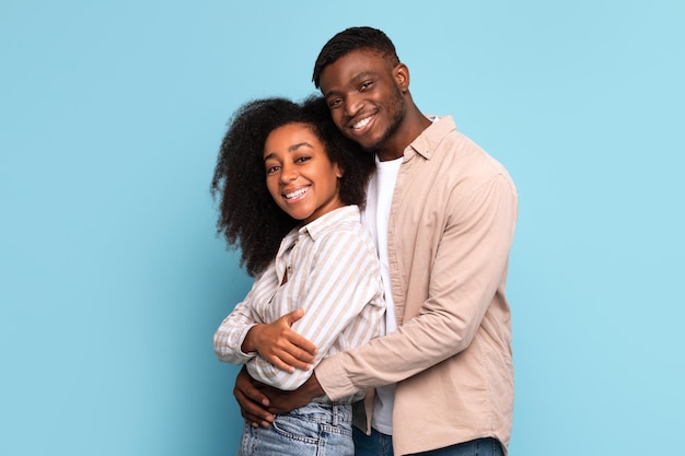 Una pareja negra enamorada se abraza con sonrisas brillantes en azul