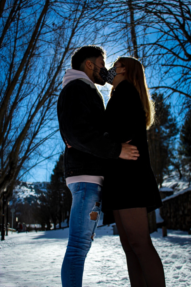 Foto pareja en la nieve en un día soleado en un bosque con árboles y cielo azul