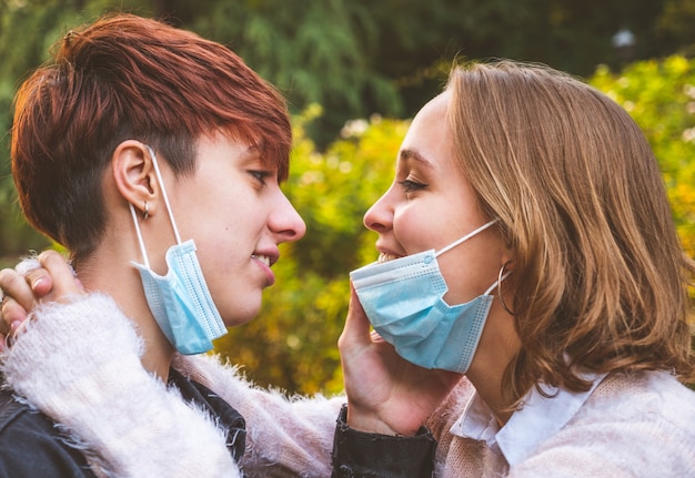 Pareja de niñas con máscara abrazando mirándose a los ojos en un parque