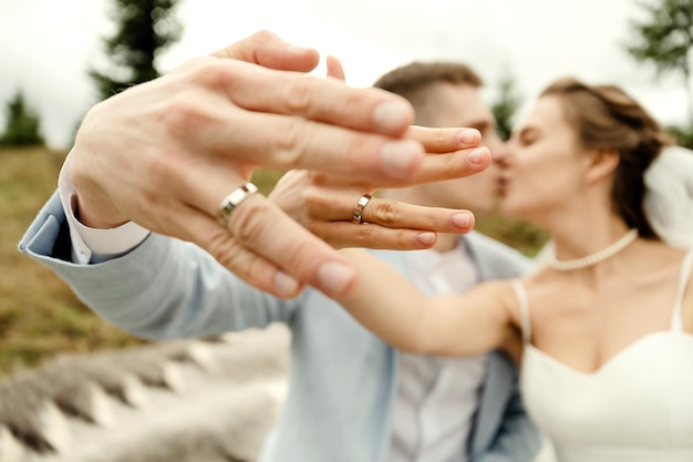 Una pareja de novios alegre y creativa sentada en una colcha en las montañas muestra sus anillos en sus manos anillos de boda concepto de detalles de boda