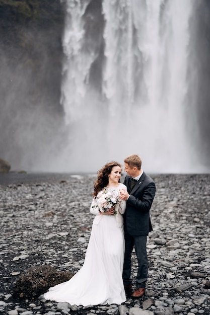 Pareja de novios cerca de la cascada skogafoss destino islandia boda el novio abraza a la novia por el