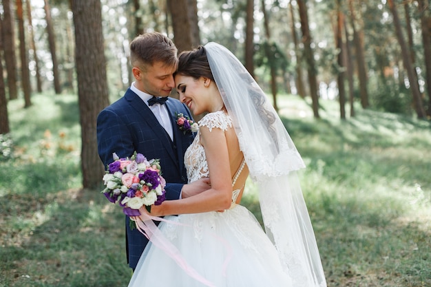 Pareja de novios emocional en el parque verde en primavera. sonriente novia y el novio en un día soleado al aire libre. felices recién casados abrazándose y besándose en el día de la boda en la naturaleza.