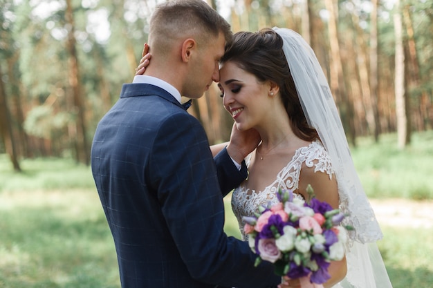 Pareja de novios emocional en el parque verde en primavera. sonriente novia y el novio en un día soleado al aire libre. felices recién casados abrazándose y besándose en el día de la boda en la naturaleza.