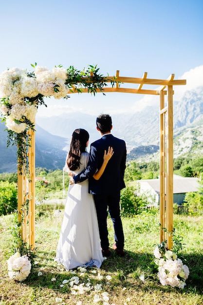 Pareja de novios de luna de miel viaje vista posterior Arco de boda montañas y fondo marino en Montenegro Estilo de boda de bellas artes