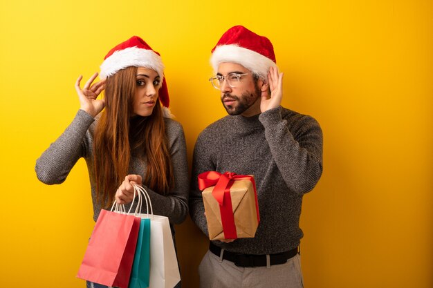 Pareja o amigos que sostienen regalos y bolsas de compras intentan escuchar un chisme